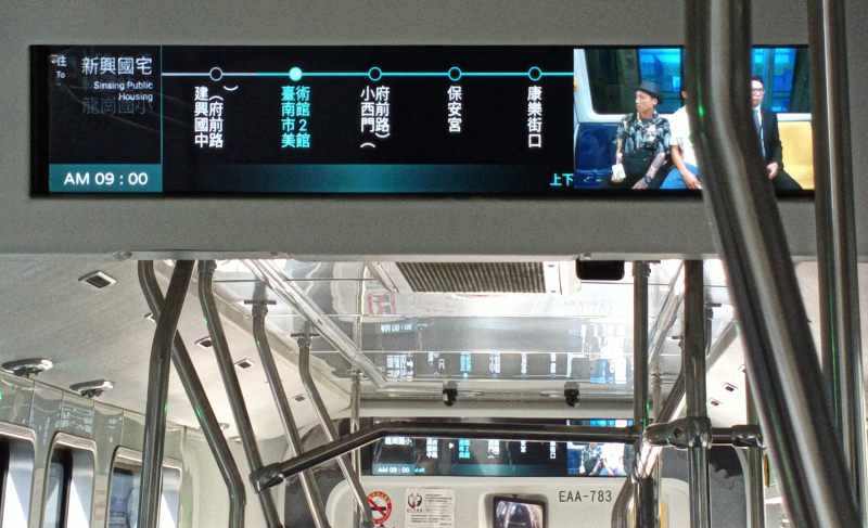 公車內部靠近車頂處的全彩顯示數位式動態行程資訊看板特寫，部分內容被公車車廂內的扶桿遮擋